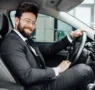 handsome young businessman full suit smiling while driving new car 95x90